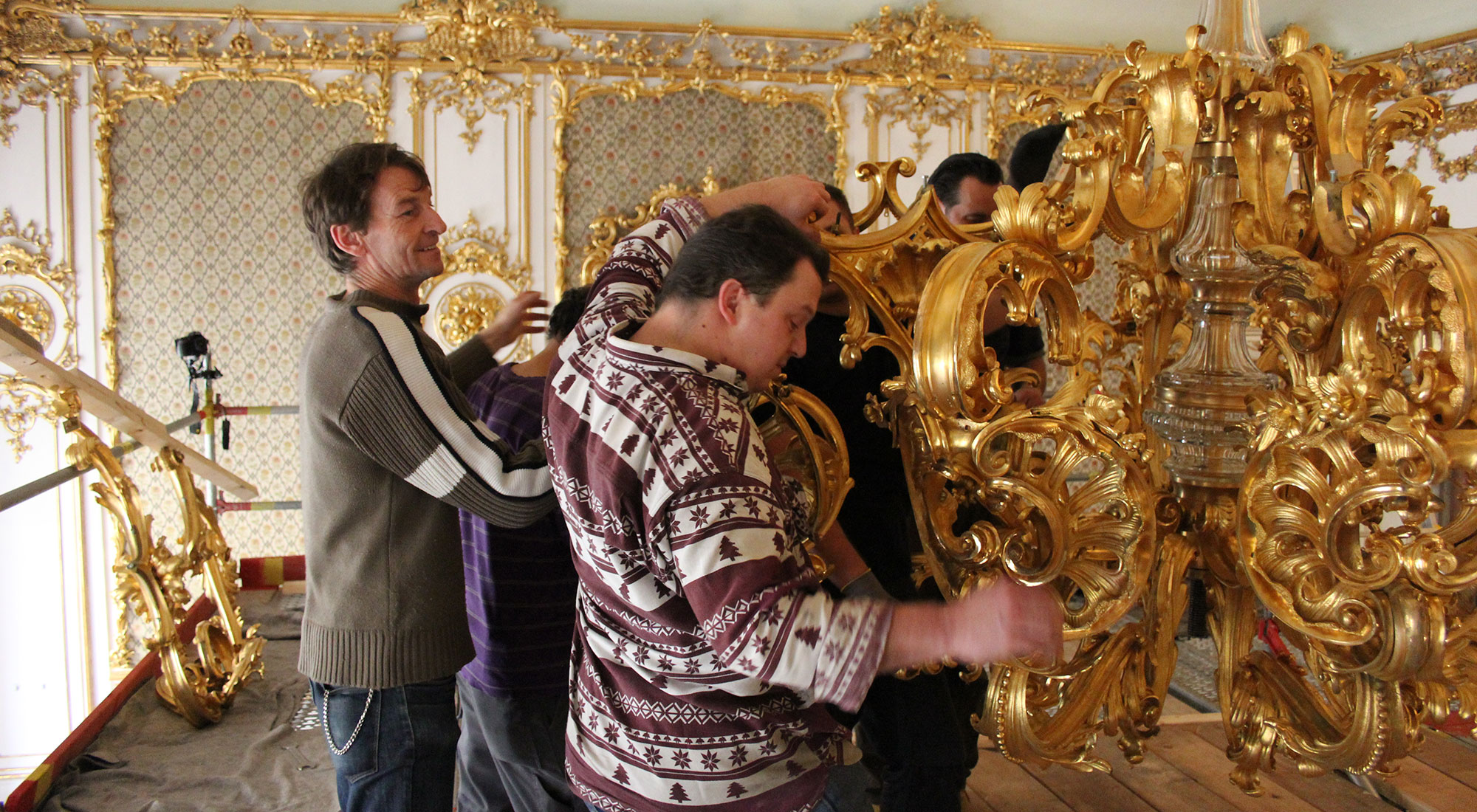 Massive cast and gilded brass parts being attached on the chandelier